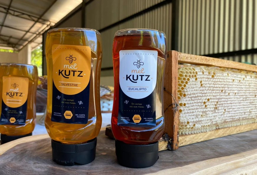 Bisnagas de mel Kutz silvestre e eucalipto ao lado de um quadro de favo